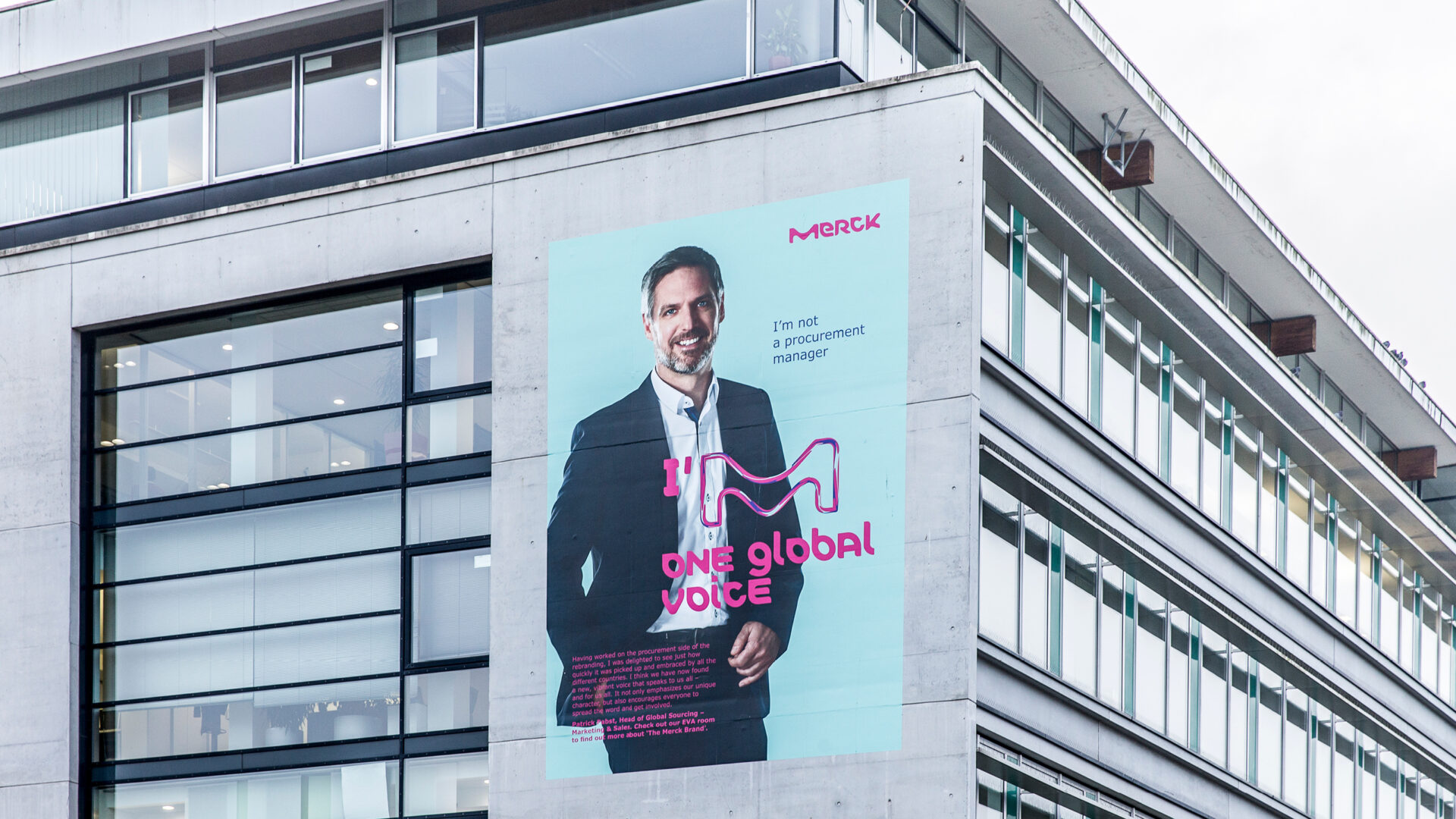 Zwei Stockwerke hohes hellblaues Plakat mit dem Portrait eines Merck Mitarbeiters an einem Werksgebäude