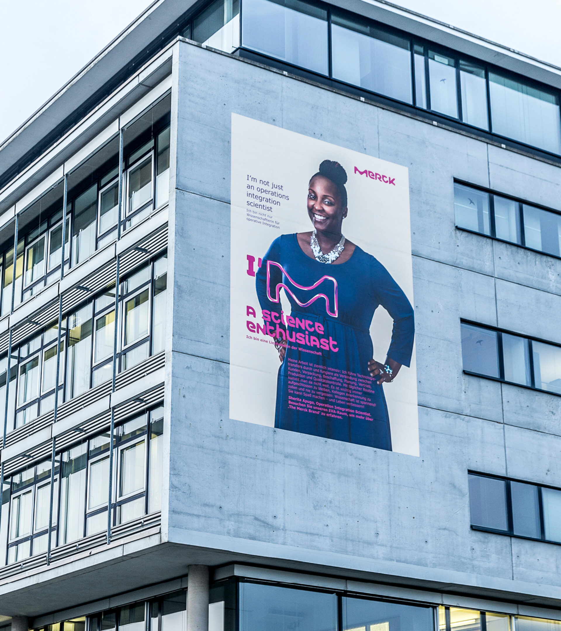 Zwei Stockwerke hohes beiges Plakat mit dem Portrait einer Merck Mitarbeiterin an einem Werksgebäude