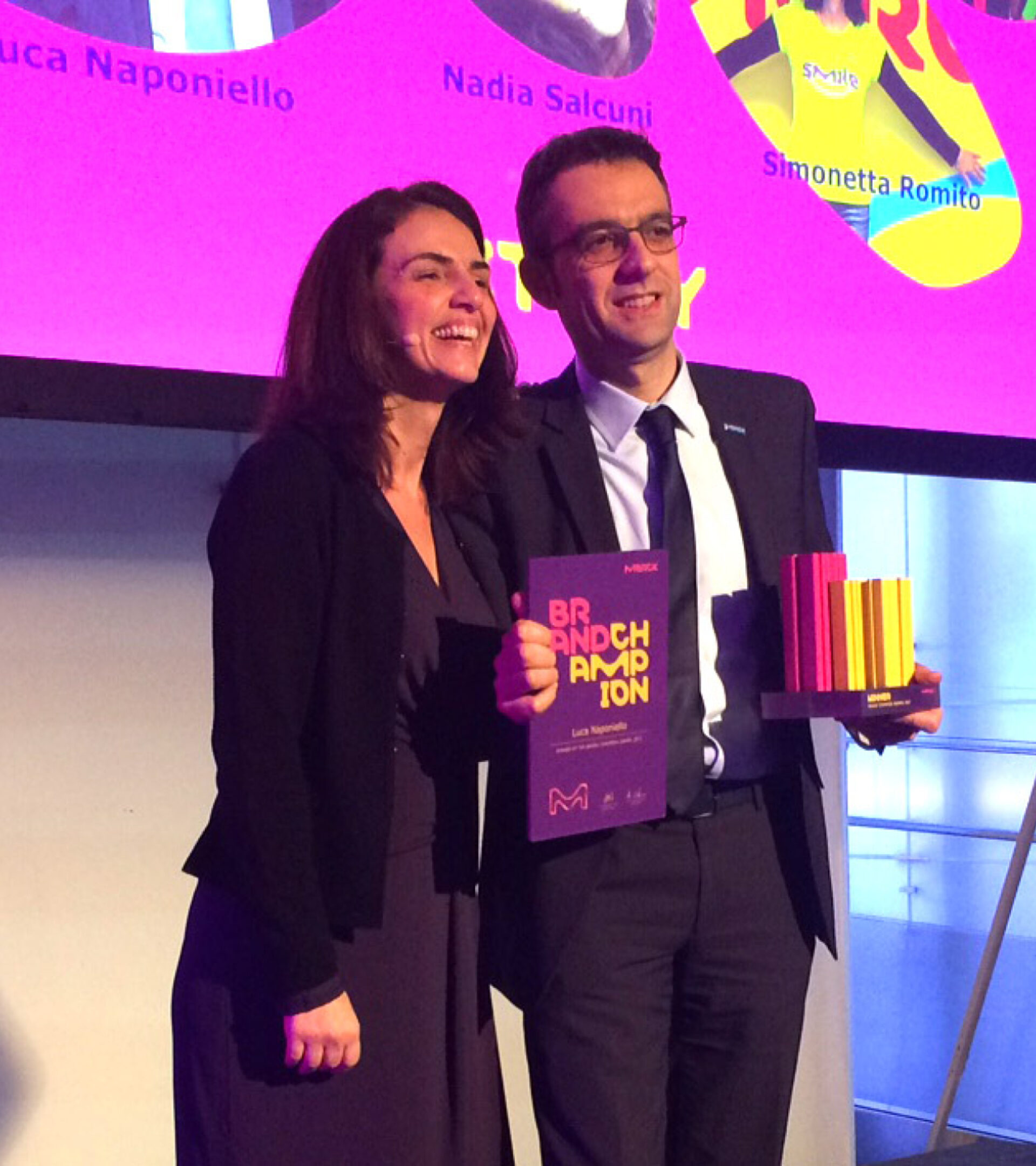 Zwei Personen halten den violett-gelben Brand Champion Award und die Auszeichnung